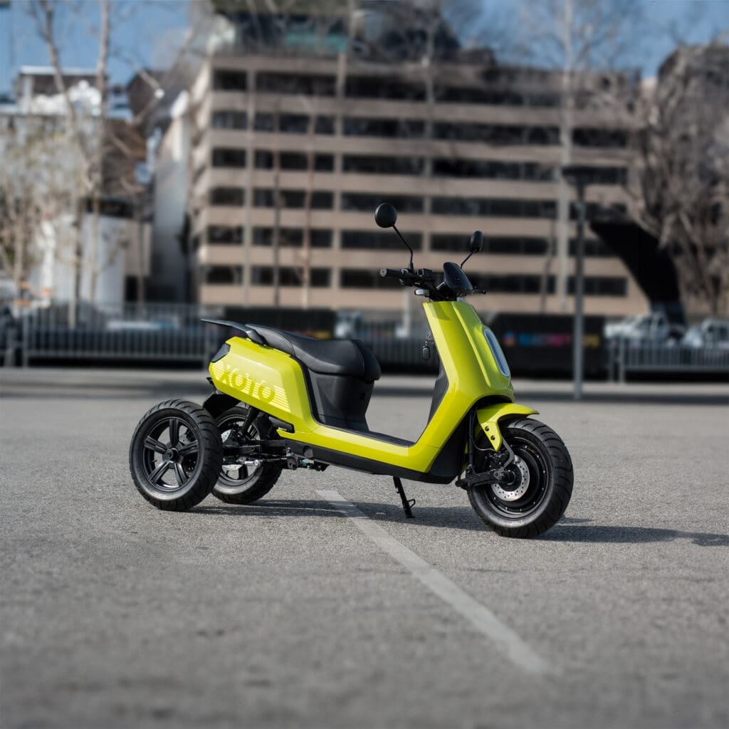 Green XOTO 3-wheeled electric scooter in parking lot of city building