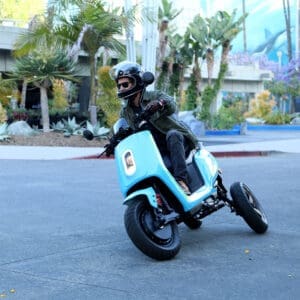 Front view of rider on blue XOTO 3-wheeled leaning electric scooter